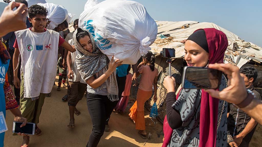 Saudi entrepreneur Adwa Al-Dakheel carries a UNHCR aid package at Kutupalong camp, Bangladesh while being filmed by Dubai-Palestinian YouTuber Haifa Beseisso. Photo: UNHCR/Andrew McConnell