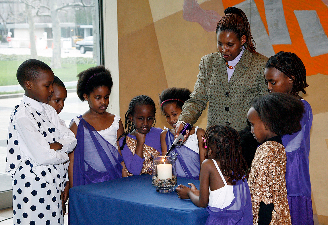 Eugenie Mukeshimana, Rwanda genocide survivor, flanked by children of Rwanda, lights a memorial candle.