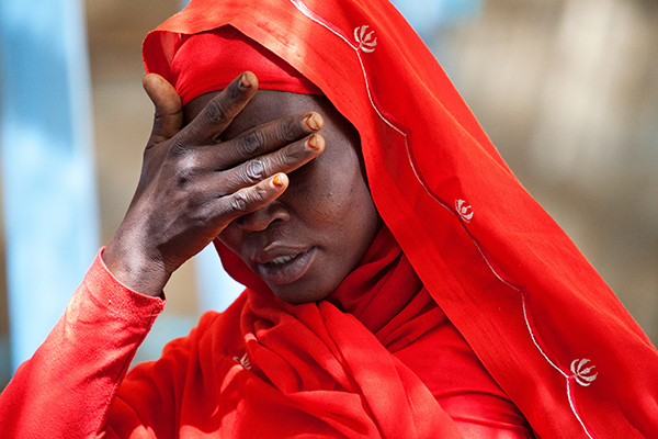 A woman crouches her head and covers her face with her hand.