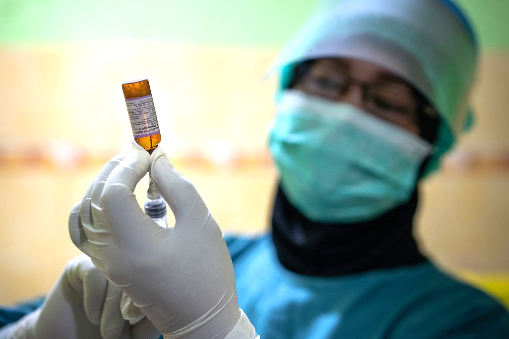 A healthcare worker transfers the vaccine from the vial to a syringe. 