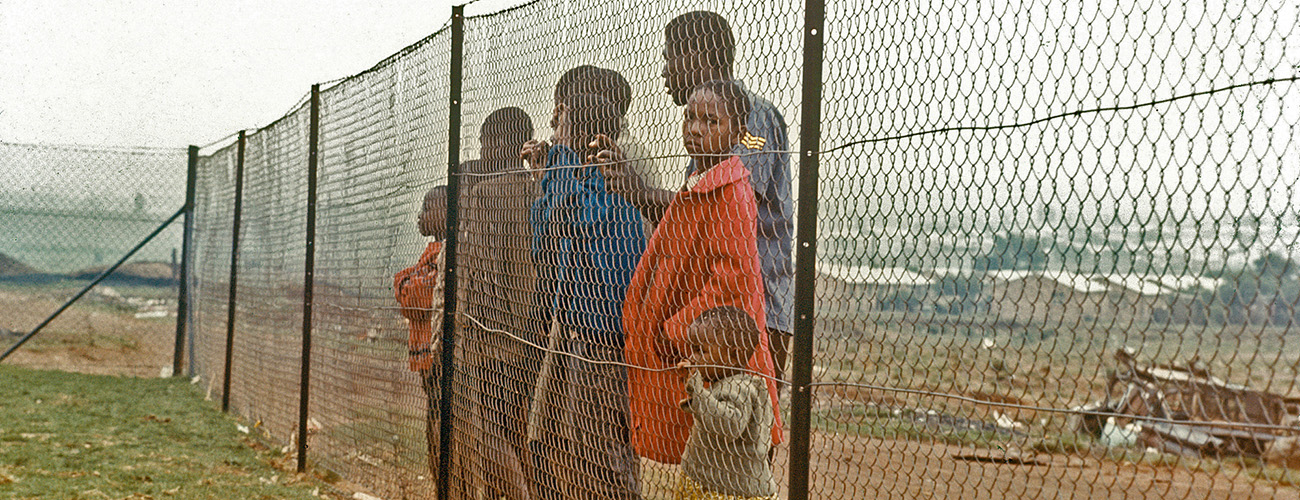 A group of people including many children standing behind a fence.