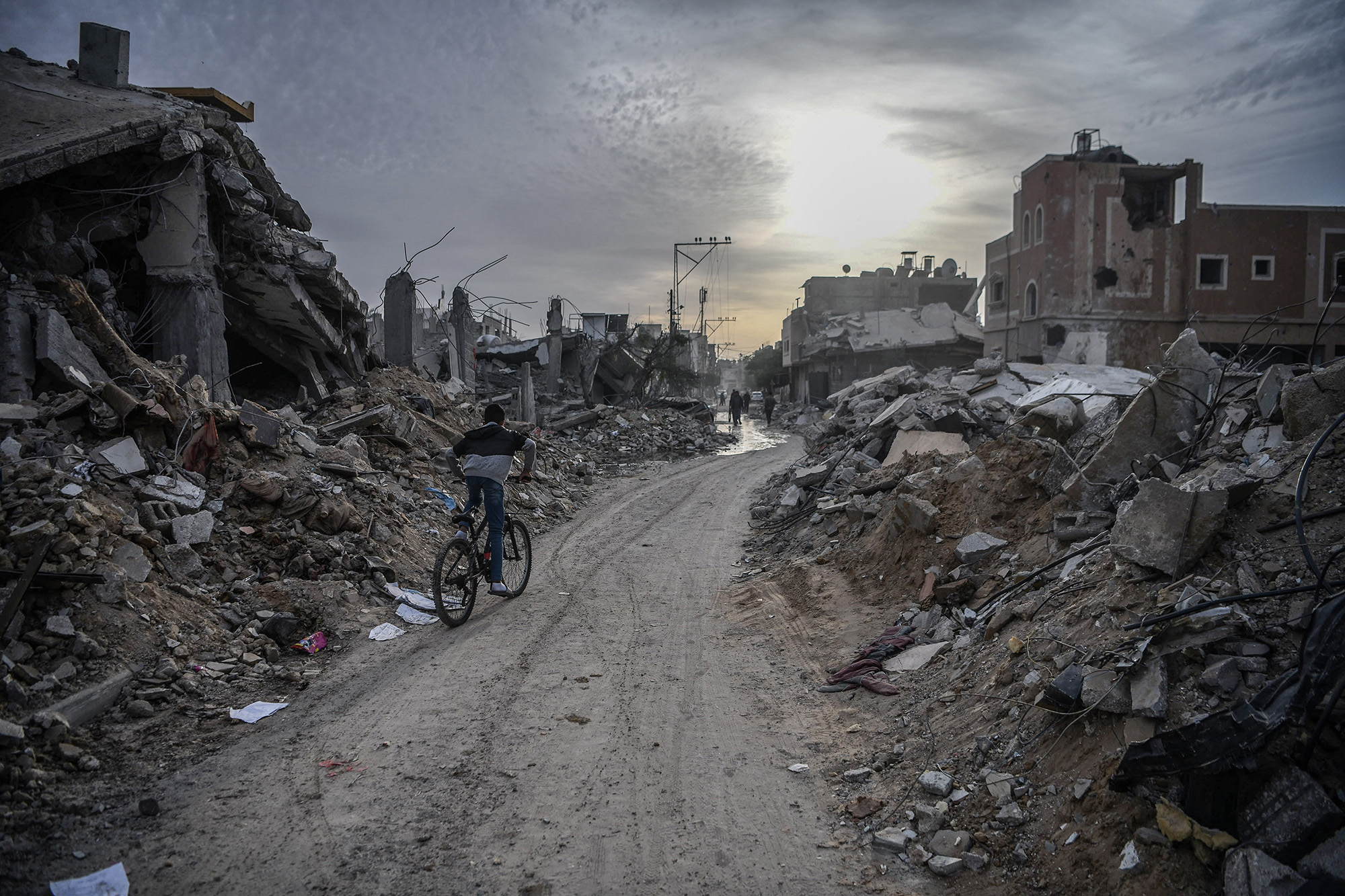Un jeune garçon à vélo traverse un groupe de maisons détruites à Gaza.