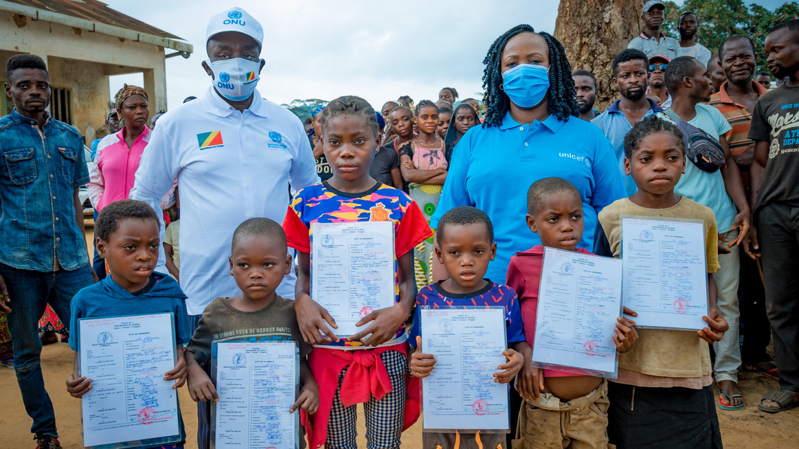 Chris stands with children who hold their birth certificates