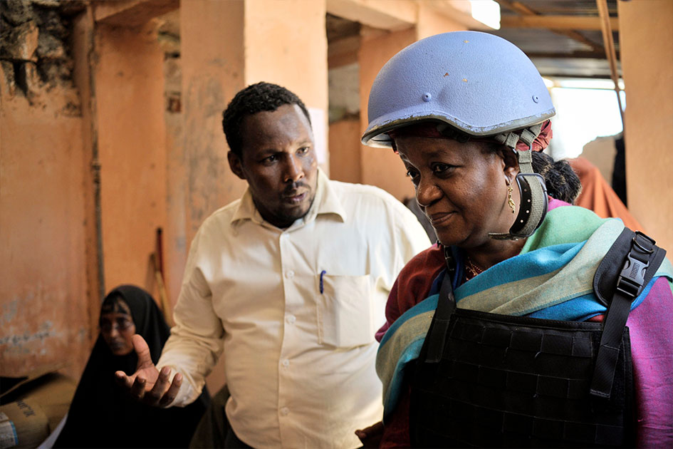 A man speaks to Ms. Bangura. She is wearing a blue helmet and protective vest.
