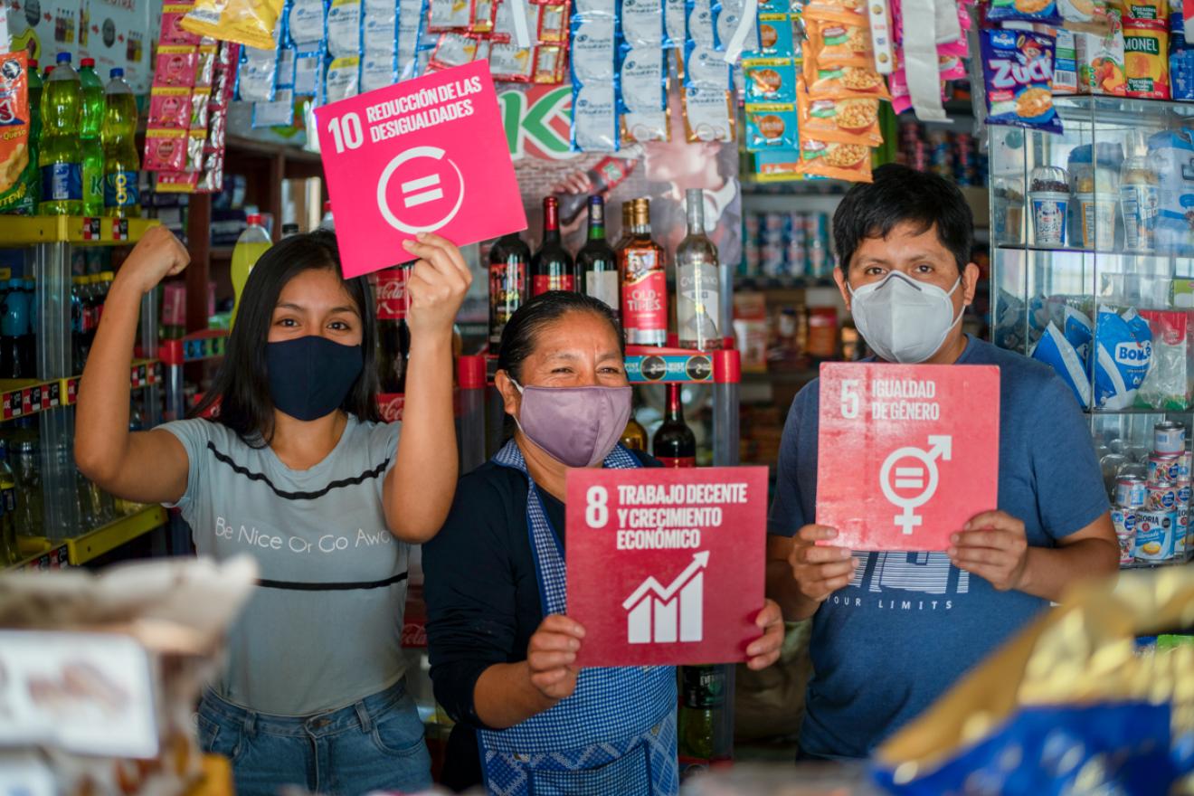 Tres personas sujetan carteles de diferentes ODS en una tienda en Perú.